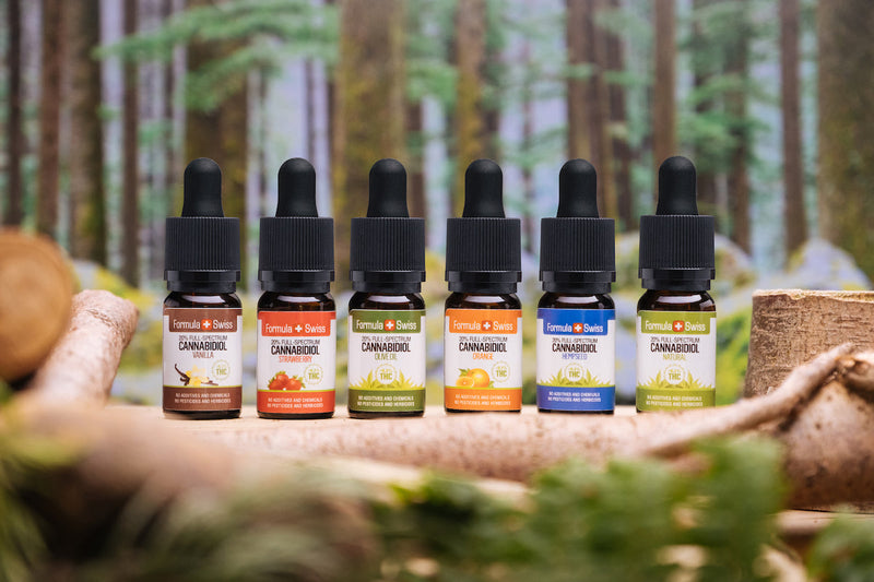 Six huiles de CBD à spectre complet Formula Swiss, dans différentes huiles de support et saveurs, devant une forêt
