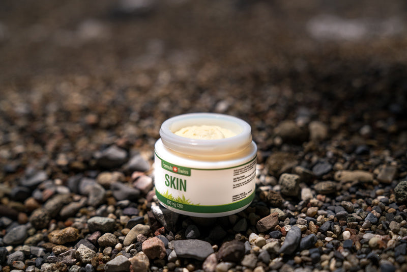 Pot ouvert de baume CBD Skin de Formula Swiss, 300 mg de CBD, sur une plage de galets
