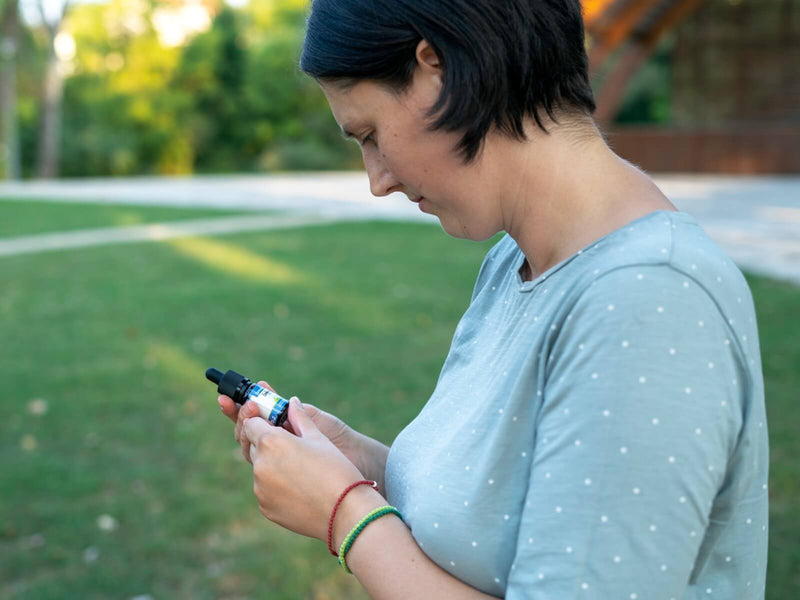 Femme regardant un flacon d’huile de CBD Formula Swiss dans sa main, en extérieur