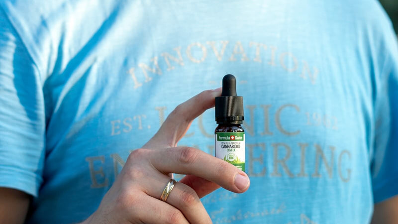 Une main tenant un flacon de 10 ml d’huile de CBD Formula Swiss dans de l’huile d’olive