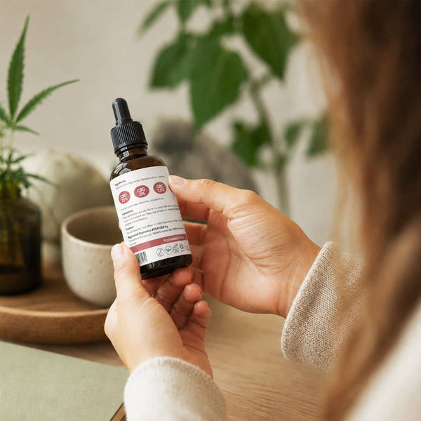 Femme examinant l'étiquette sur une bouteille d'huile de cannabinoïde de Formule Suisse dans un cadre intérieur lumineux.